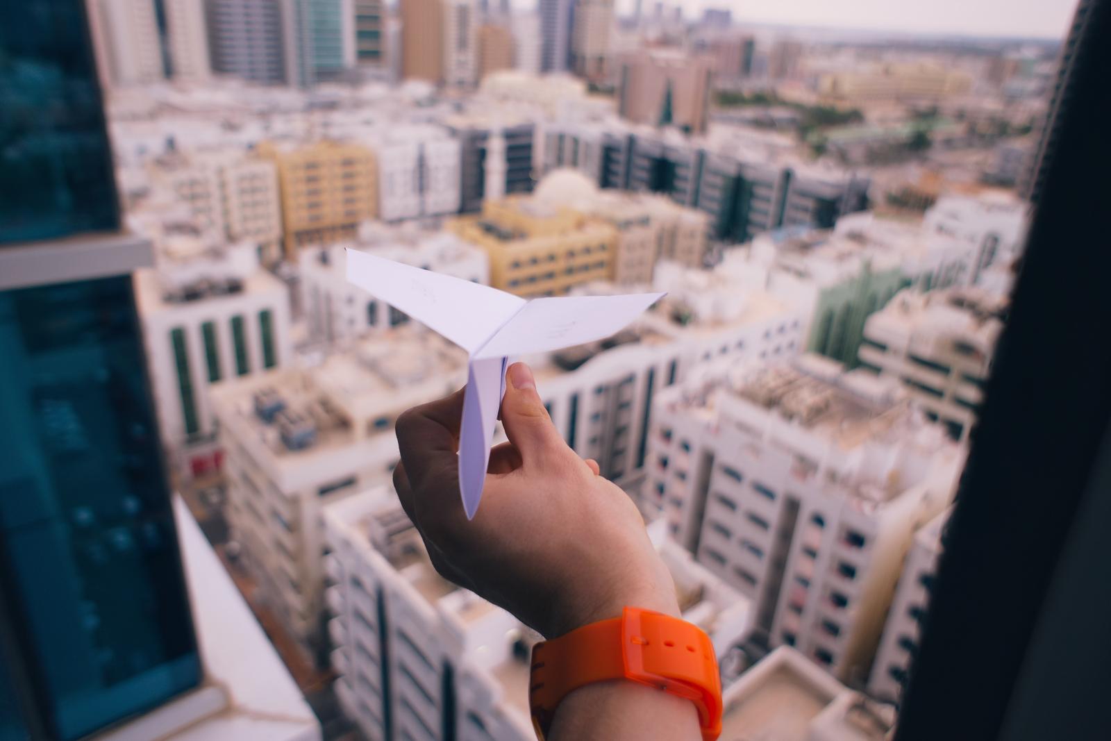 main tenant un avion en papier à la fenêtre d'un immeuble