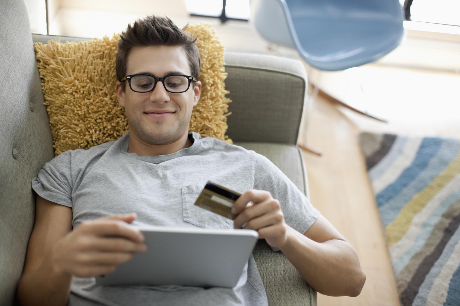homme allongé sur un canapé effectuant un paiement par carte en ligne sur son pc
