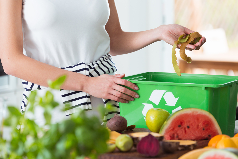 Femme recyclant les déchets de cuisine biologique en compostant dans un récipient vert pendant la préparation du repas