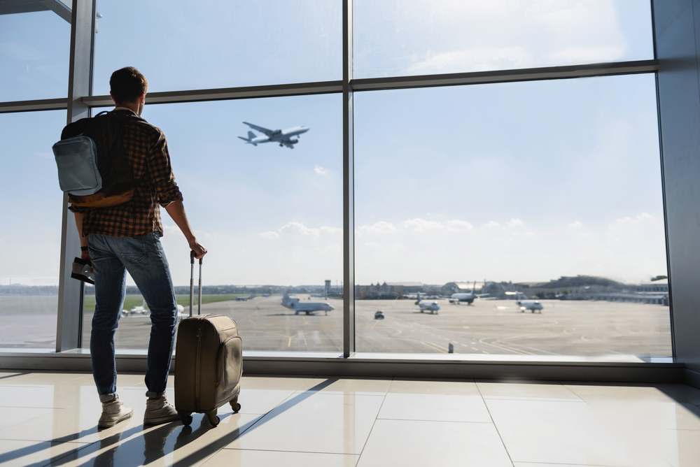 Jeune homme se tient près de la fenêtre à l'aéroport et regarde l'avion avant le départ.