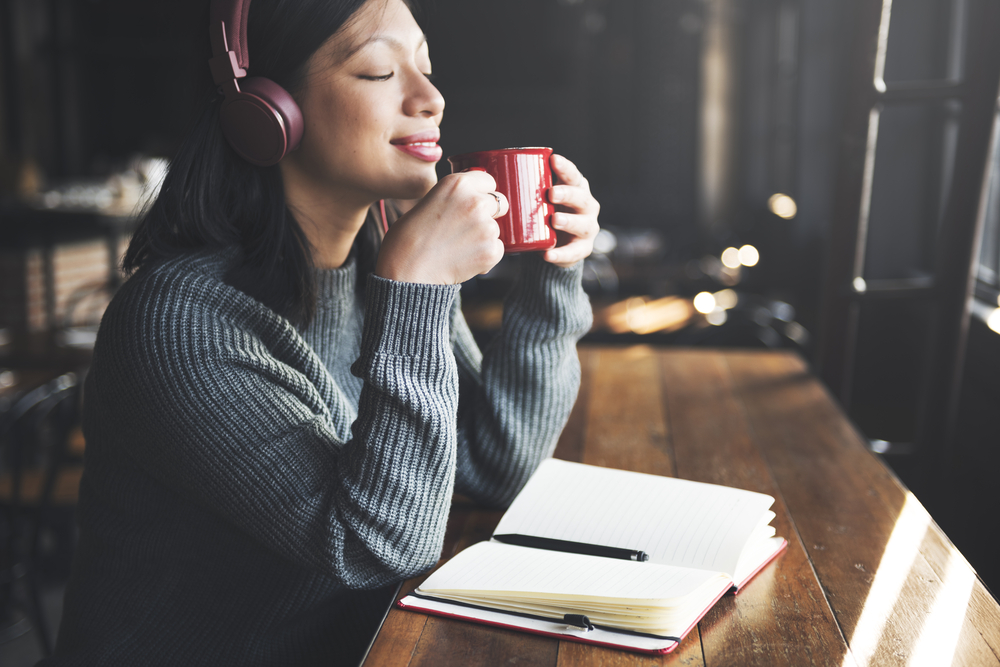 Femme écoutant de la musique en buvant un café devant un carnet ouvert